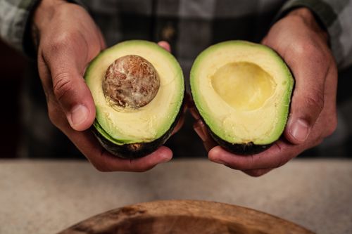 Free High angle of crop anonymous male demonstrating ripe halved avocado while standing at table Stock Photo