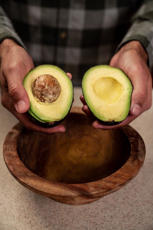 Free Close-up of hands holding avocado halves above a wooden bowl, perfect for food photography. Stock Photo