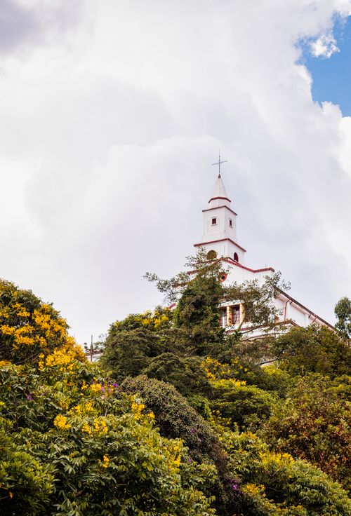 Free A beautiful view of Monserrate Church steeple surrounded by lush greenery under a cloudy sky in Bogotá, Colombia. Stock Photo