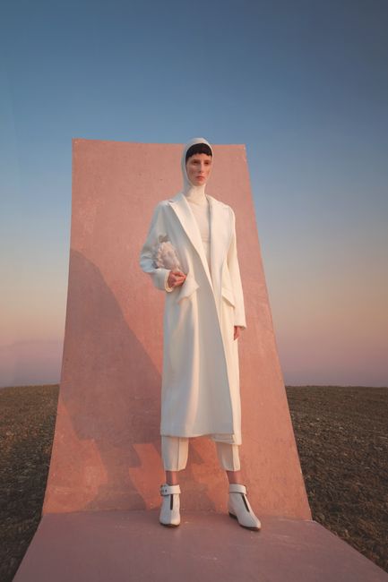 Stylish fashion model posing in a white coat outdoors at sunset, blending elegance with a modern aesthetic.