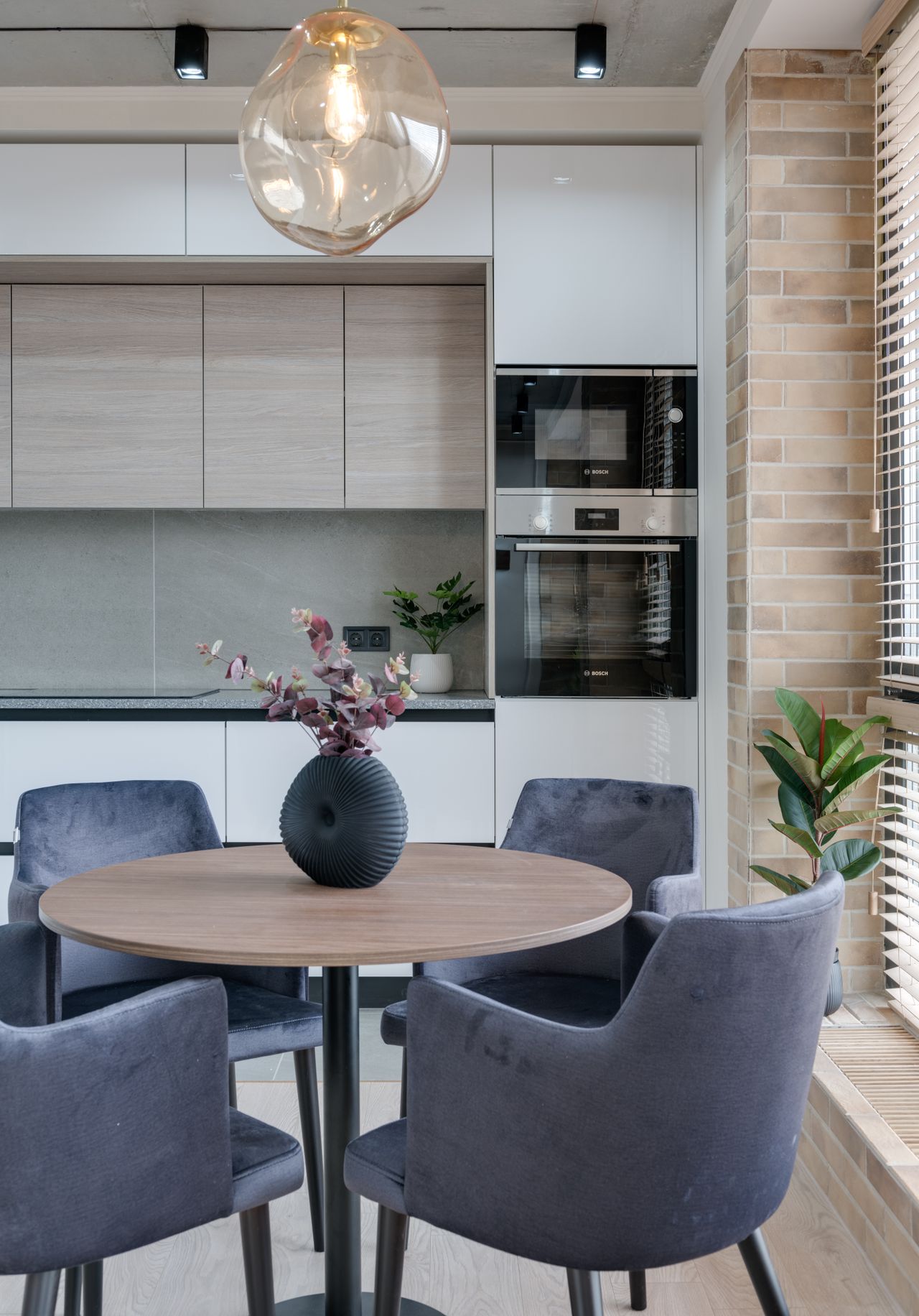 Round wooden dining table with grey velvet chairs in a kitchen