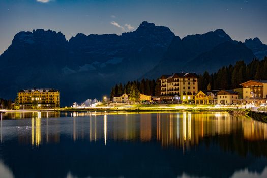 Scenery of peaceful pond surrounded by dwelling houses on shore against mountains in highland at night