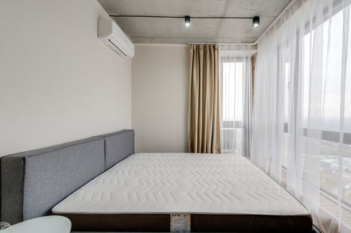 Free Spacious modern bedroom with a clean mattress and large windows for natural light. Stock Photo