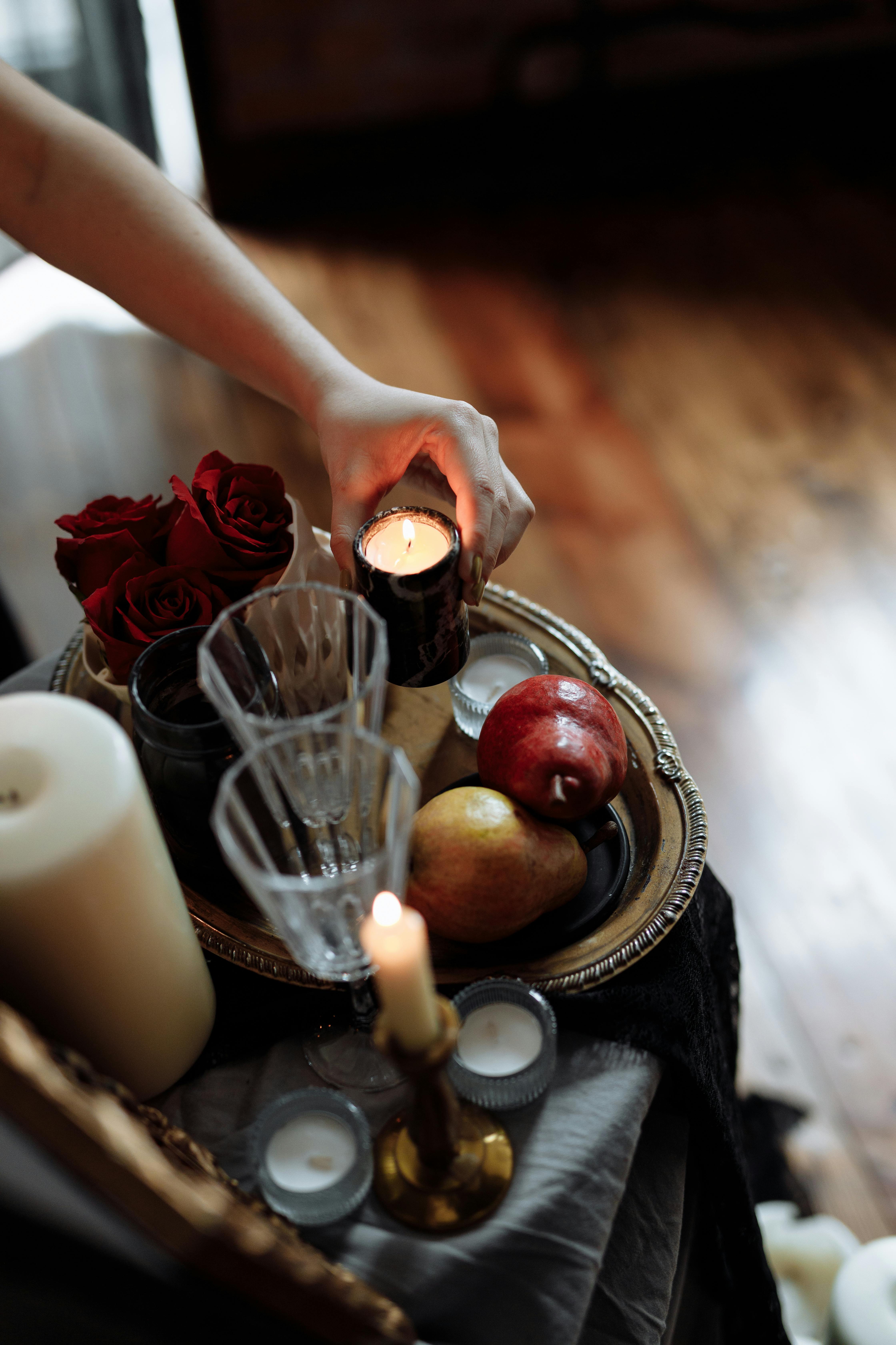 A sophisticated candlelit still life featuring fruit, roses, and crystal glasses on a silver tray.