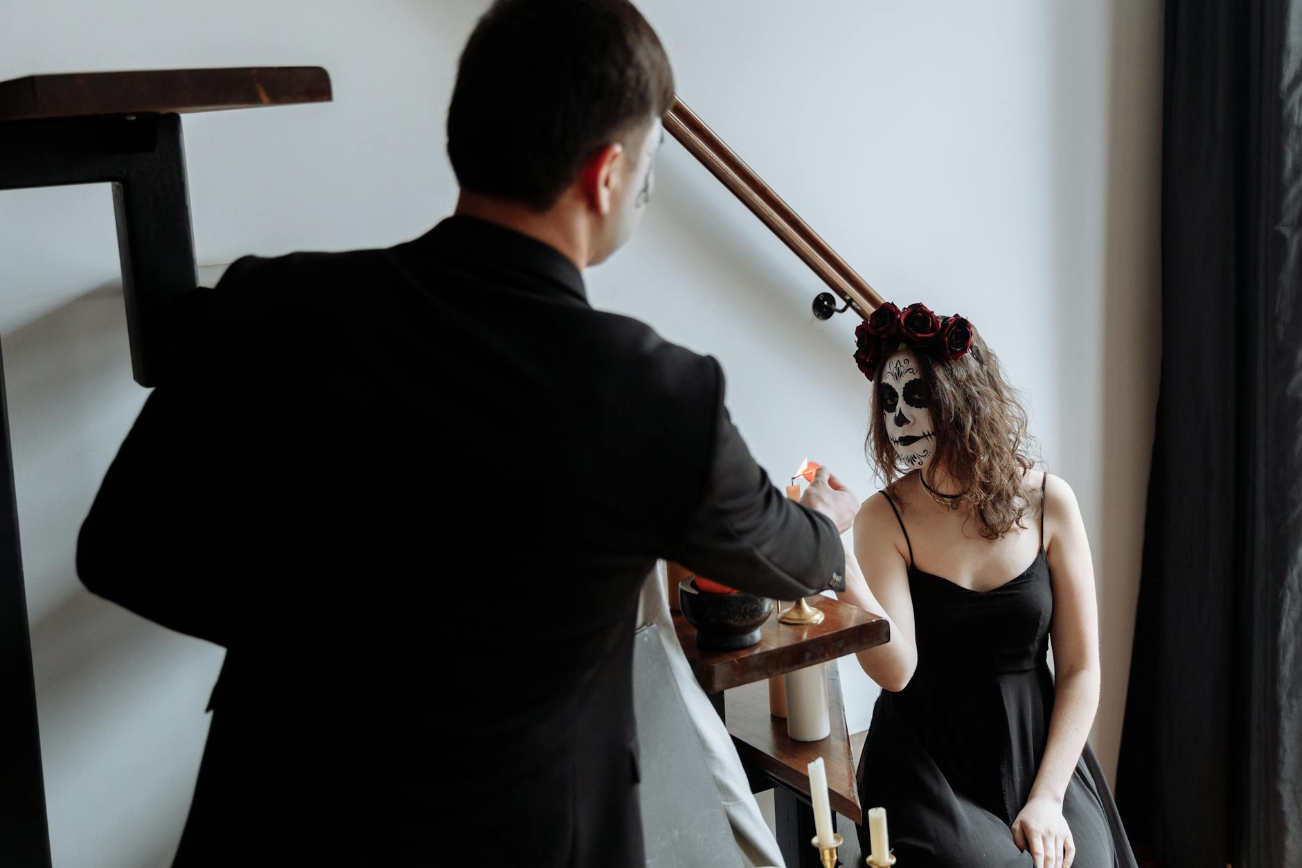 A couple celebrates Day of the Dead with traditional face paint and attire, indoors.