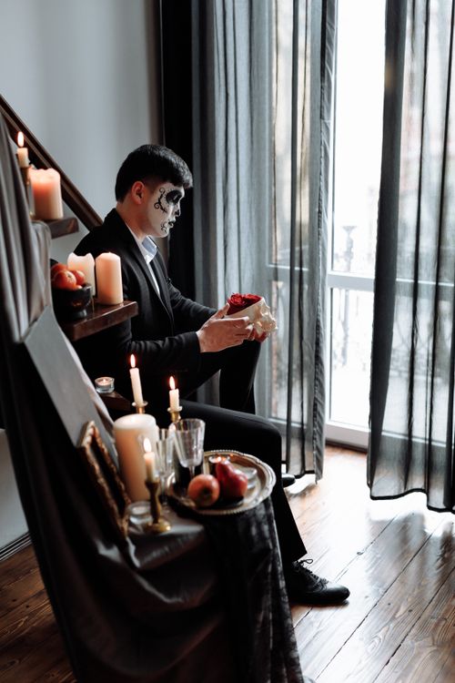 Free Dia de los Muertos themed Halloween scene with a man in makeup holding red roses. Stock Photo