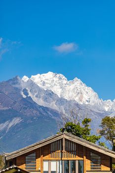 Snowy mountain view beyond a wooden house under a clear blue sky in daylight.