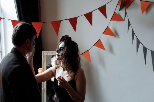 Free A woman in face paint prepares for a Day of the Dead celebration indoors with decorative bunting. Stock Photo