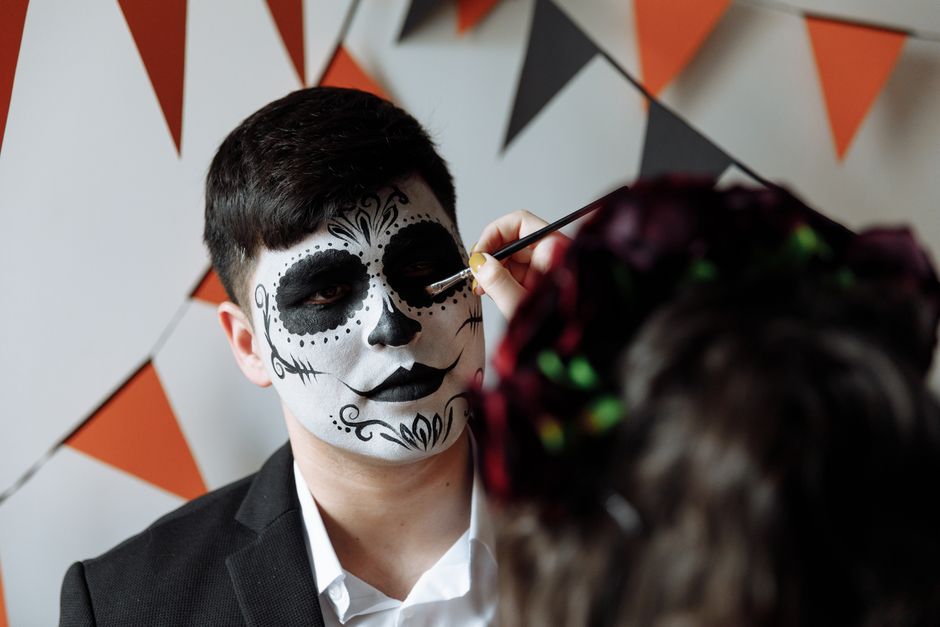 A man receives traditional face painting for Dia de los Muertos, capturing cultural heritage.