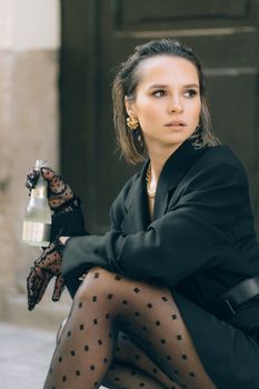 Elegant woman in black attire holding a bottled drink outdoors. Fashionable urban style.