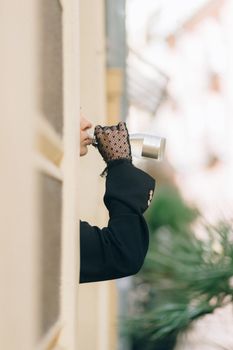 A fashionable woman in lace gloves drinks from a silver flask outdoors.