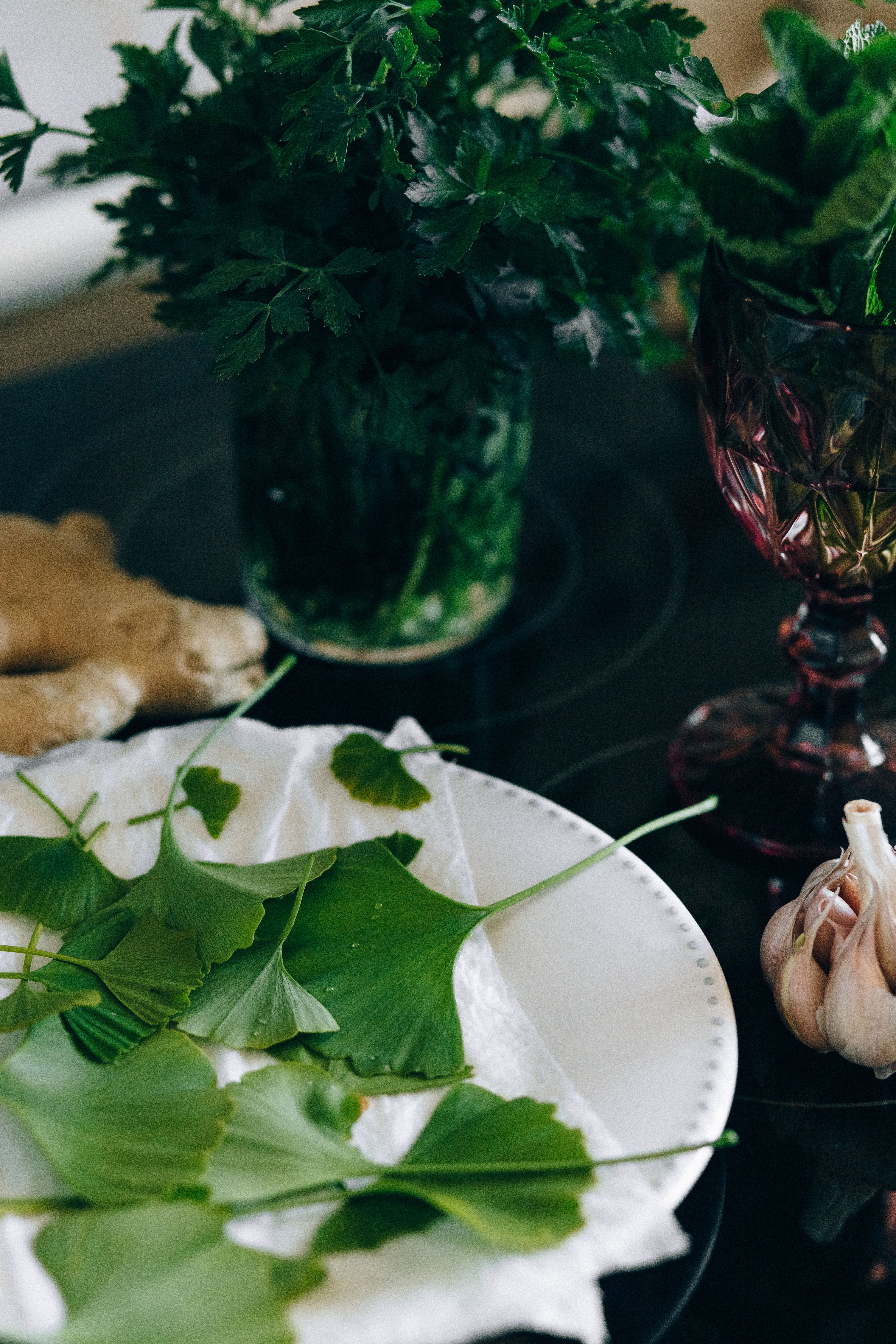 A collection of fresh green leaves and herbs with garlic and ginger on a kitchen countertop.