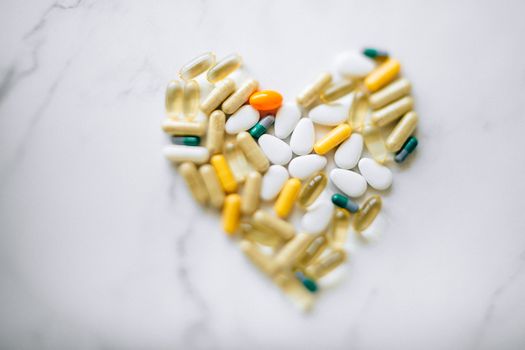 Colorful pills arranged in heart shape on a marble surface, symbolizing health and wellness.