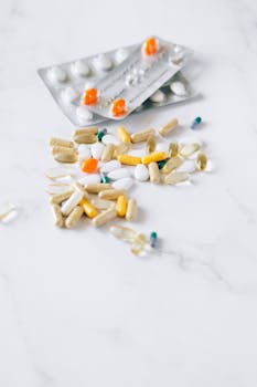 Assorted pills and capsules scattered on a white marble surface, highlighting pharmaceutical diversity.