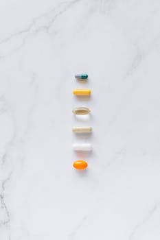 A vertical arrangement of assorted capsules and pills on a white marble background.