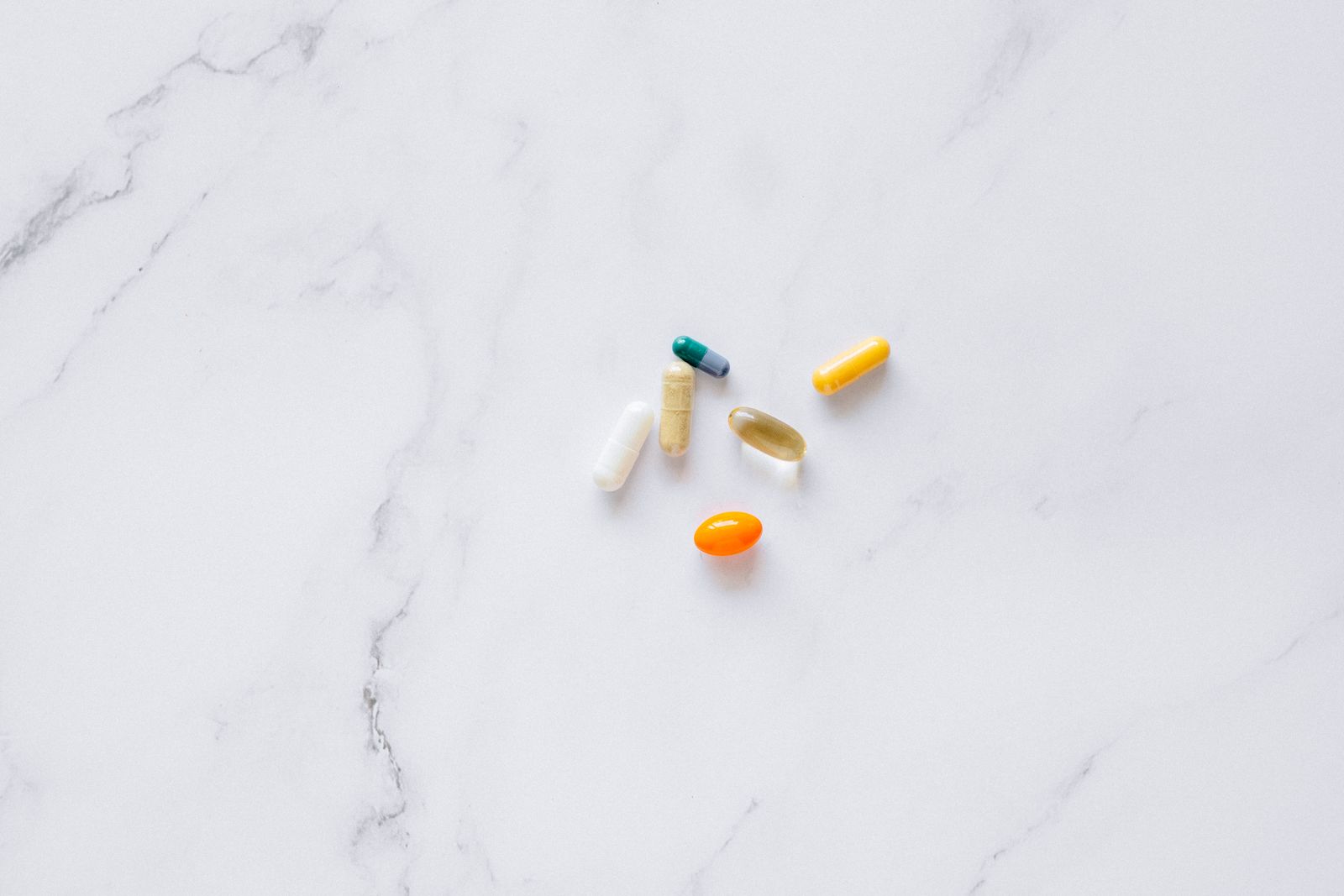 Assorted supplement capsules arranged on a white marble surface