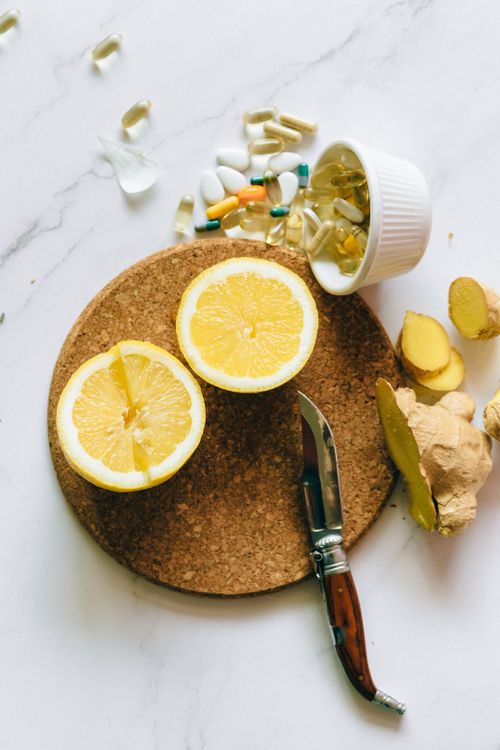 Free Flat lay of natural remedy ingredients including lemon, ginger, and supplements on a cork board. Stock Photo