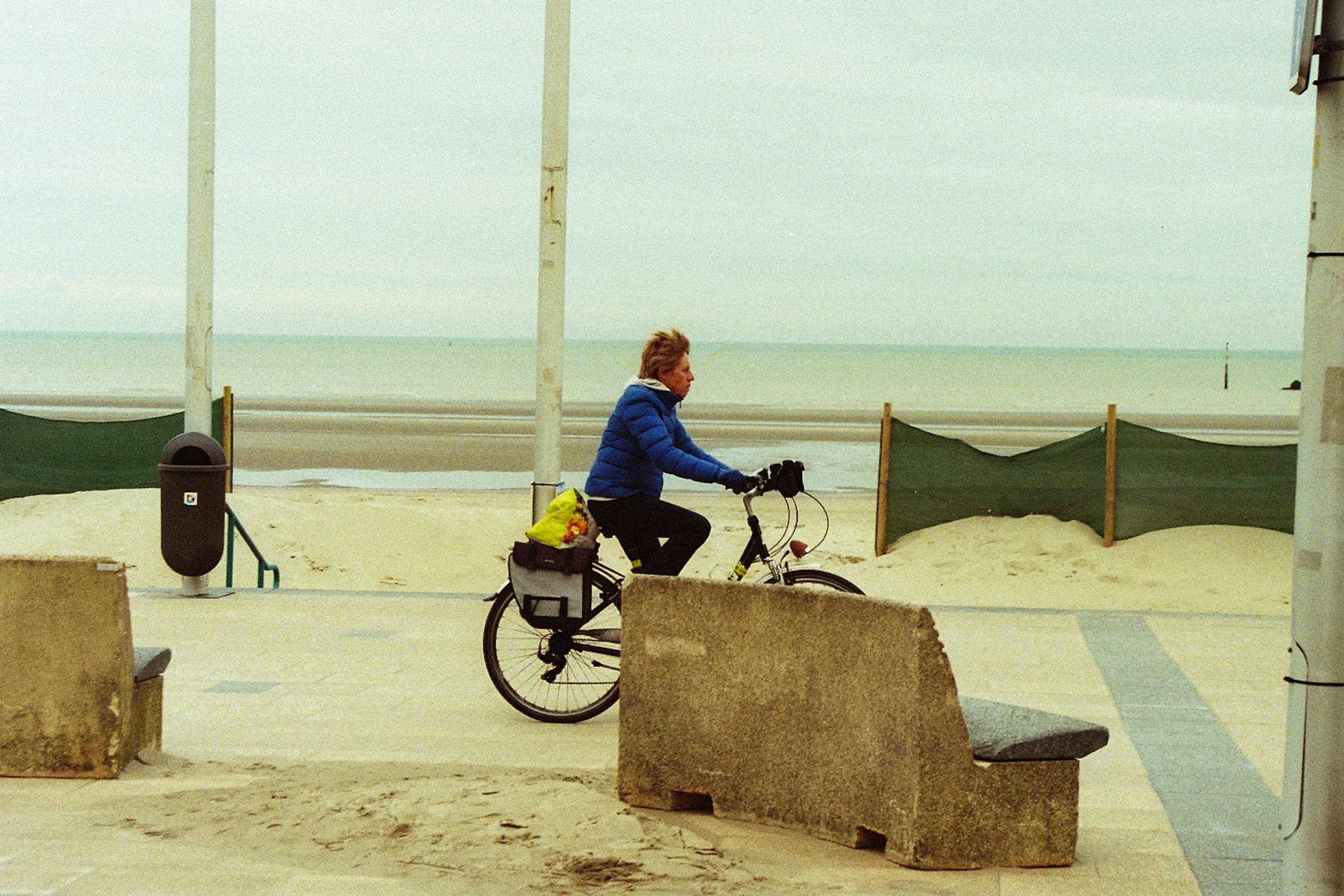 Frau fährt mit dem Fahrrad über die Strandpromenade bei Wind am Meer.