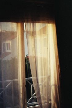 Warm sunlight filters through sheer curtains, revealing a cozy outdoor view with soft shadows.