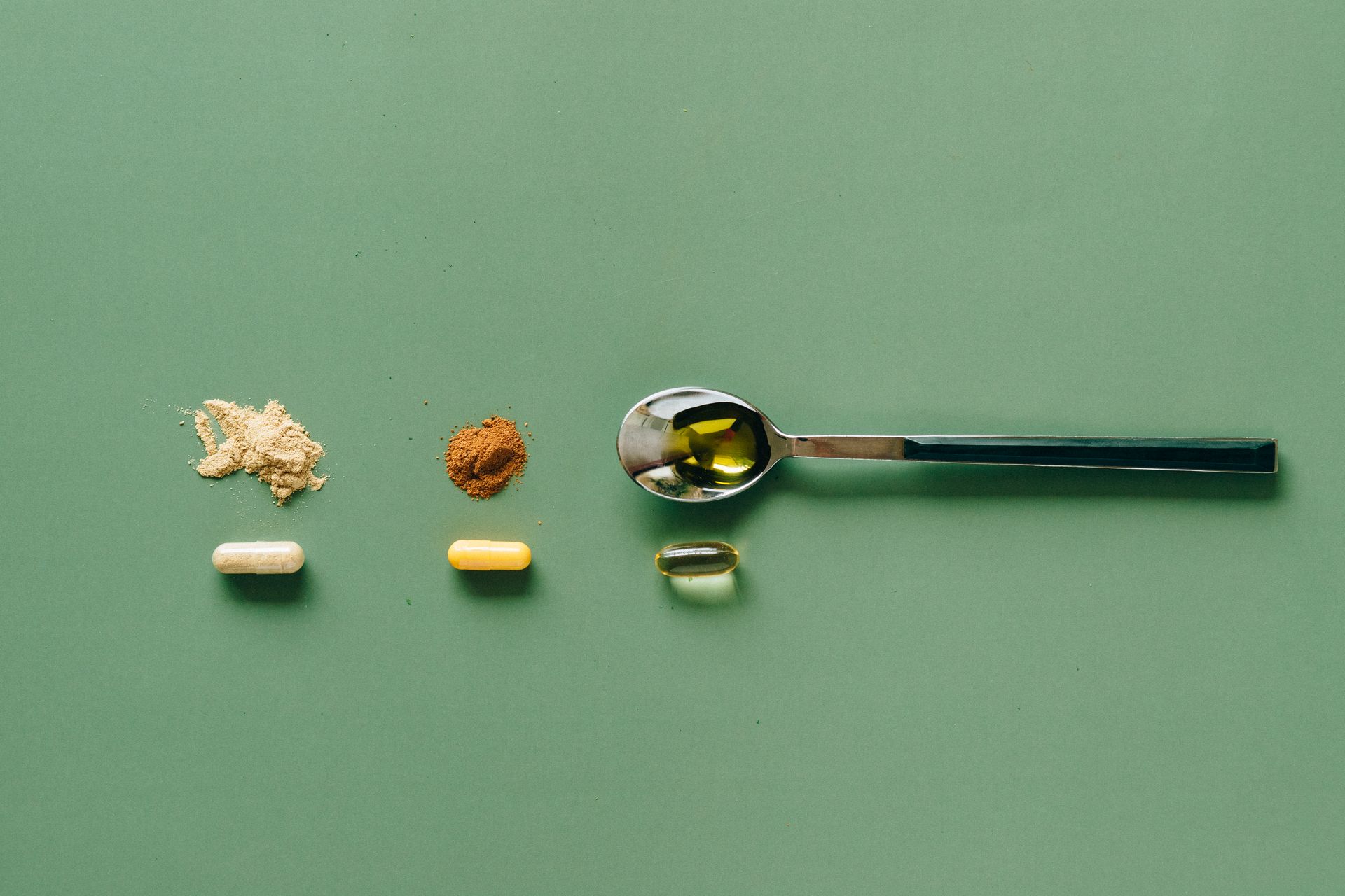 Stainless Steel Teaspoon Beside Brown Powder and Capsules