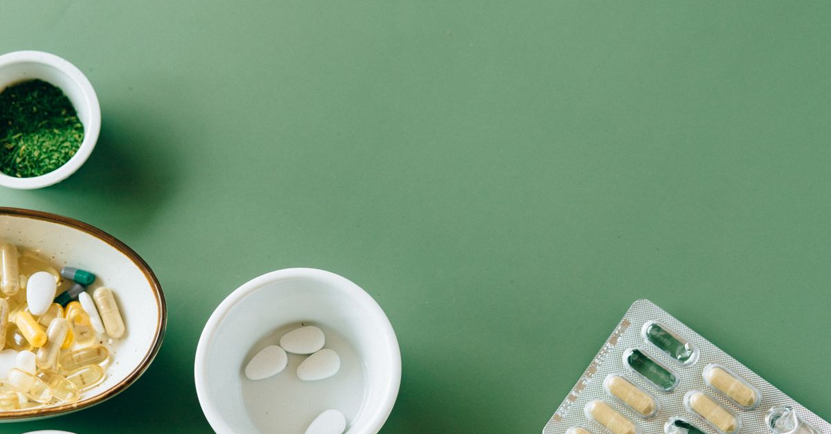 A flat lay of assorted pills and herbs on a green background emphasizing natural health remedies.