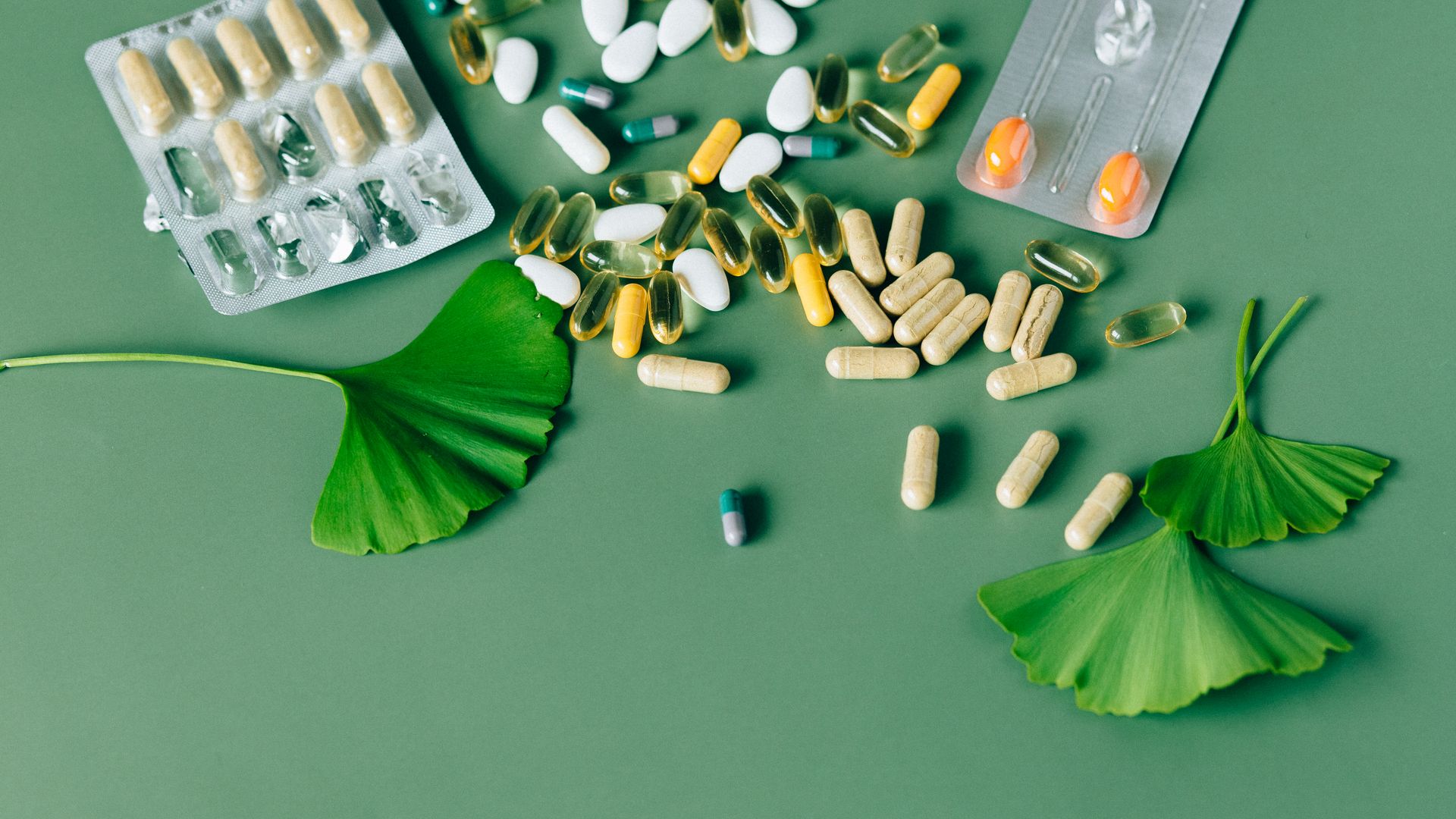 Natural Nootropics vs Synthetic: Understanding the Key Differences A variety of natural supplements and pills displayed on a green background with Ginkgo biloba leaves — natural nootropics vs synthetic