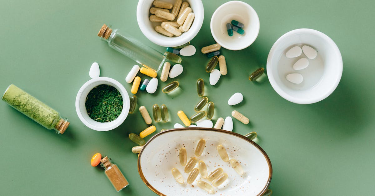 Top view of various herbal and pharmaceutical supplements in ceramic bowls on a green background.