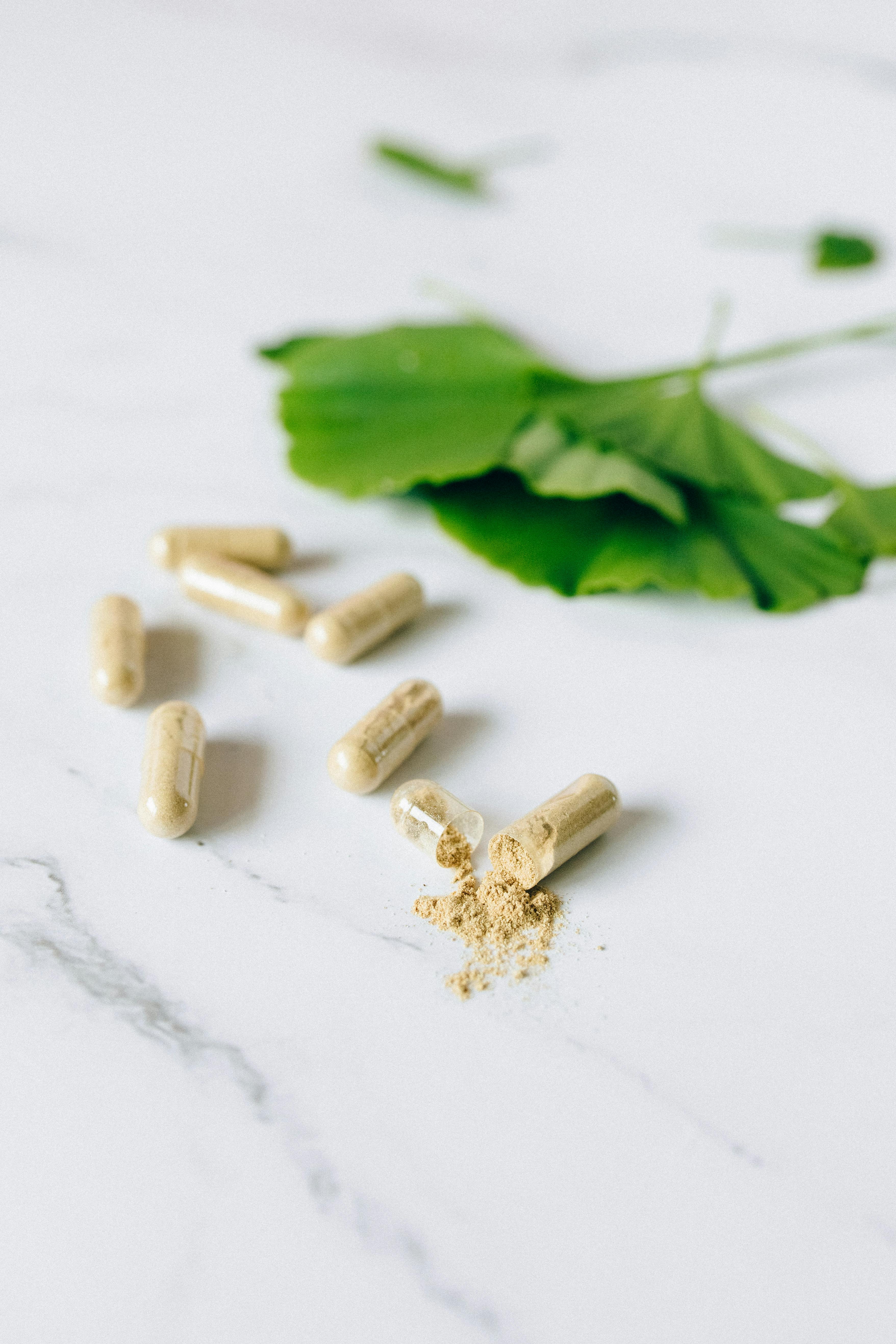 green herb and capsules on a marble surface