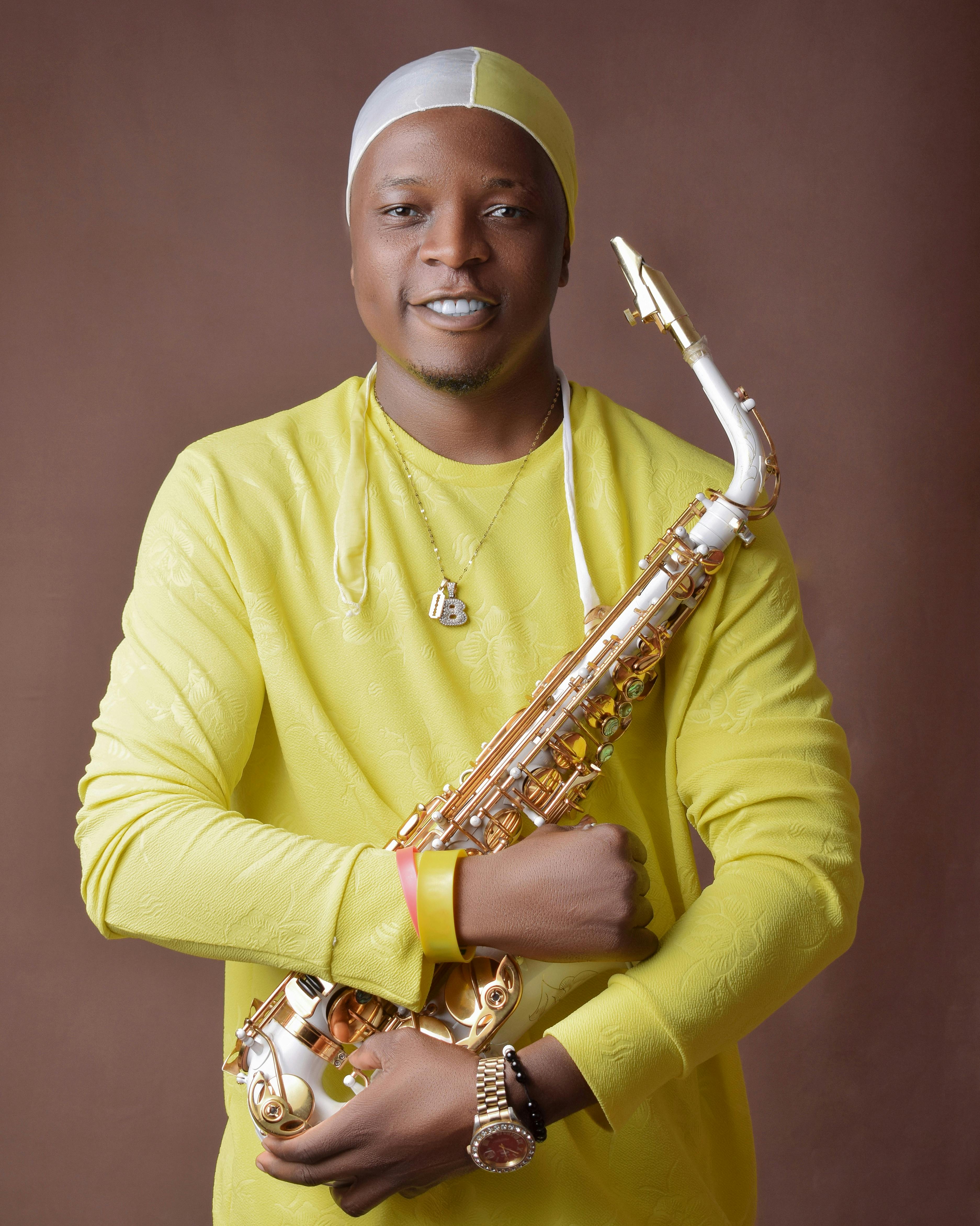 Smiling black male musician in casual clothes standing with saxophones and looking at camera against brown background