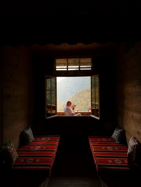 A serene scene of a person enjoying the mountain view from a rustic cabin with traditional decor in Artvin, Türkiye.