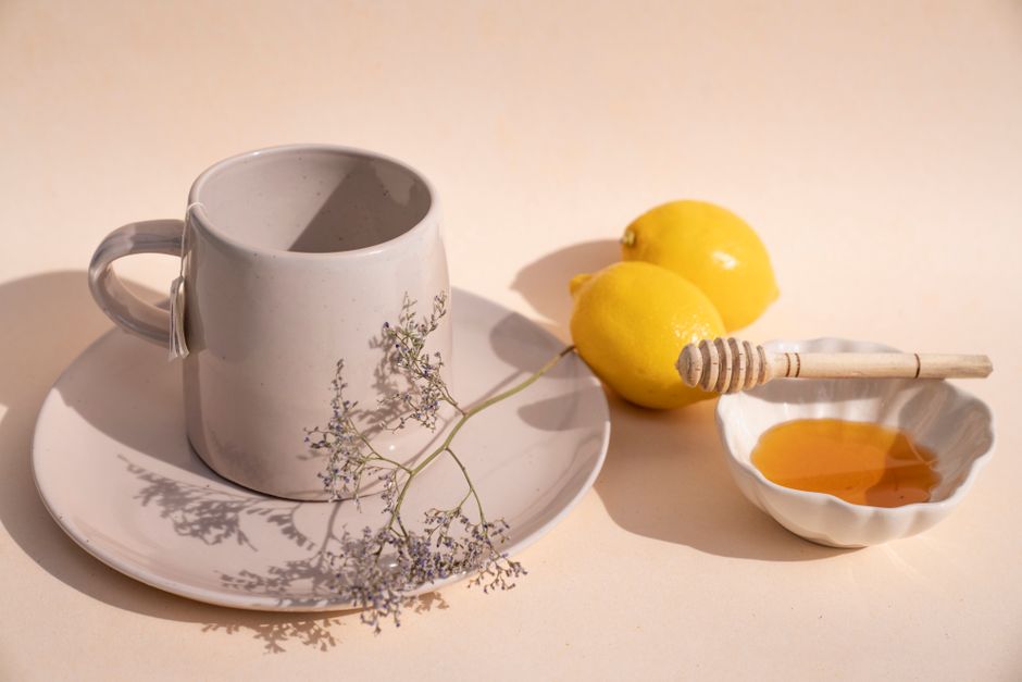 A steaming mug of amber-colored throat coat tea with a cinnamon stick and loose dried licorice root and slippery elm bark scattered on the wooden table beside it.