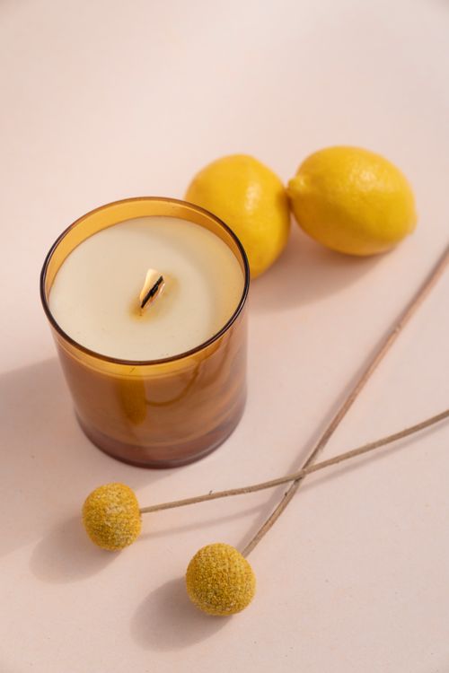 Free A warm-toned candle beside fresh lemons and craspedia flowers in a minimalist composition. Stock Photo