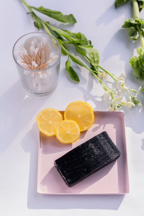 Free Flat lay of natural spa essentials featuring charcoal soap, sliced lemons, and botanical elements on a white background. Stock Photo