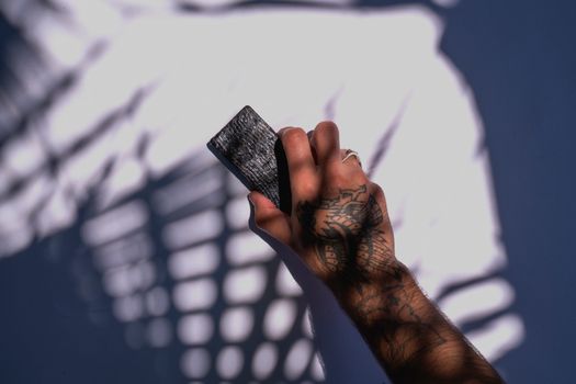 Close-up of a tattooed hand holding a skincare product with dramatic shadows creating unique patterns.