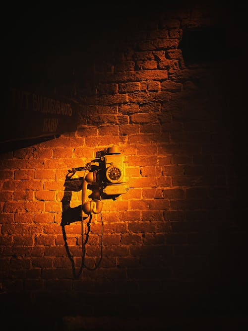 Old Telephone on Brick Wall in Yellow Spotlight