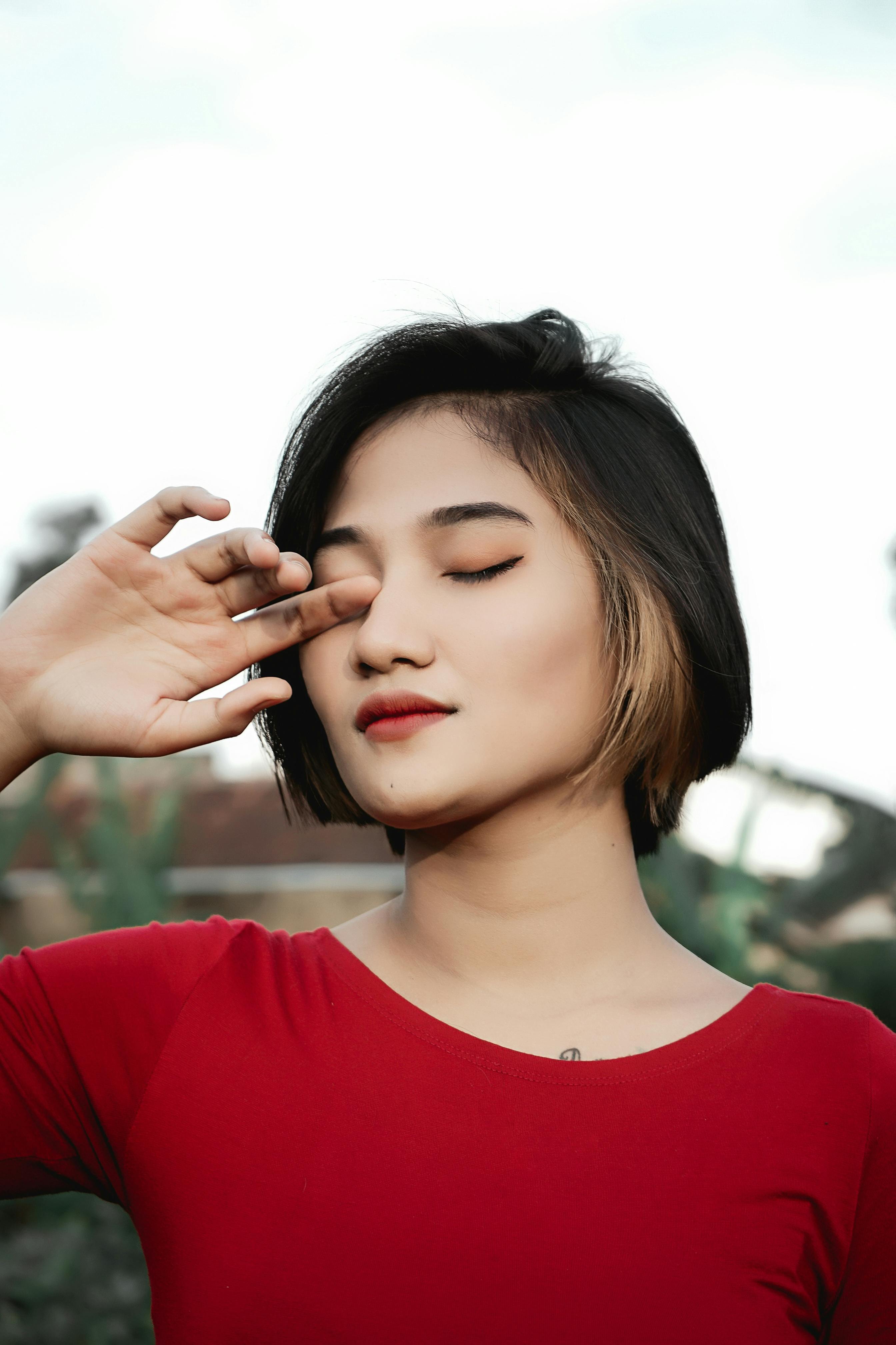 A serene portrait of a woman in a red shirt with eyes closed and hand gently touching her face.