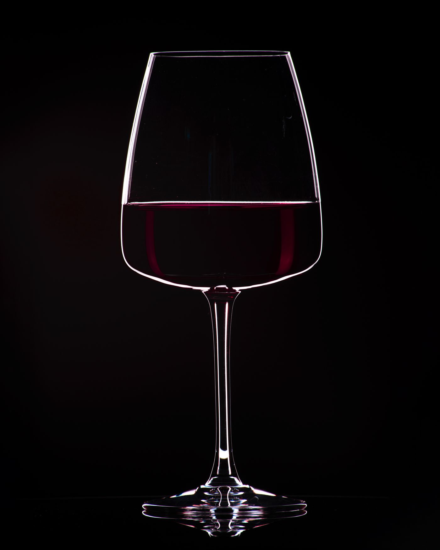 Single elegant wine glass filled with rich red wine against a minimal neutral background