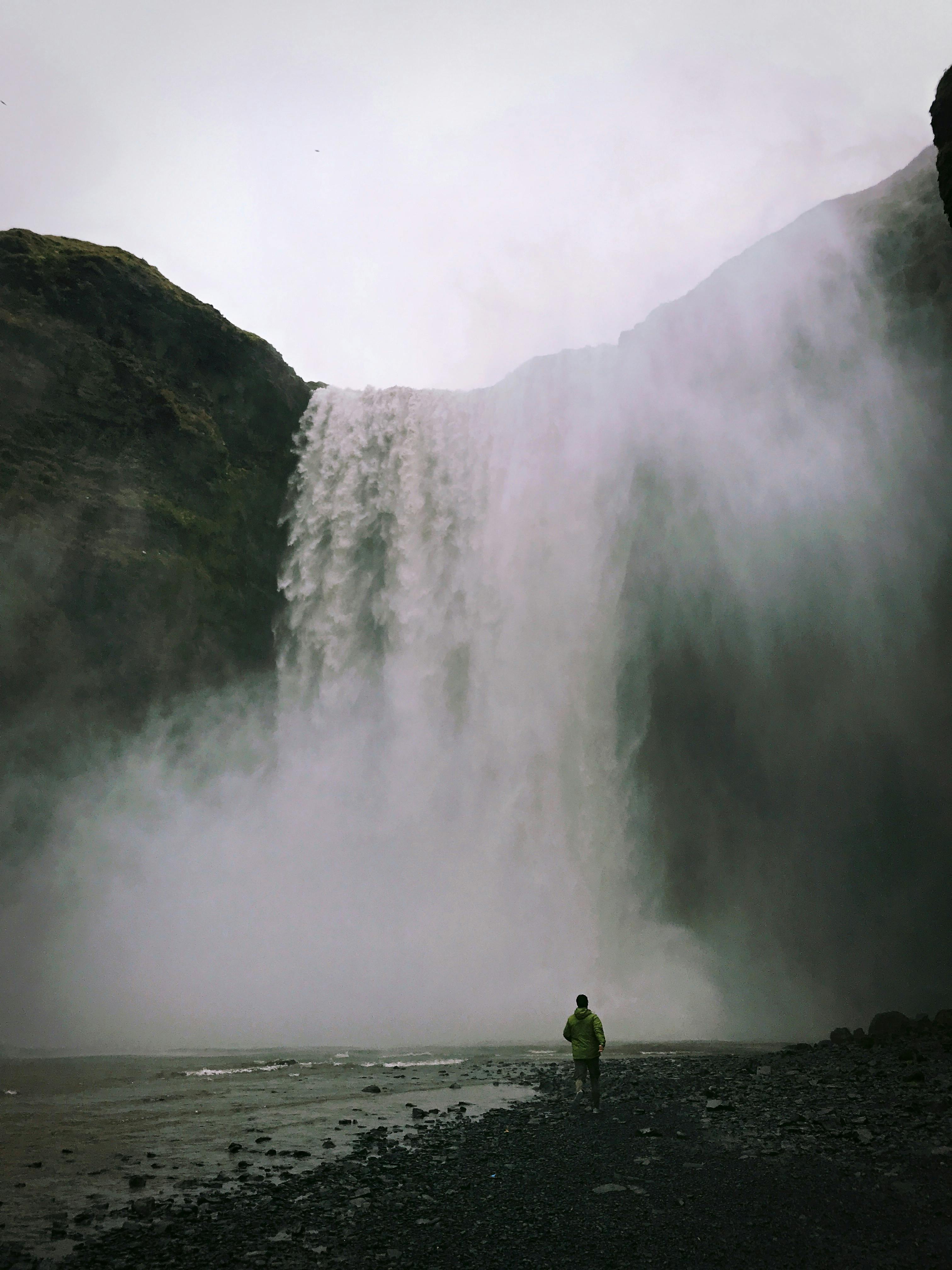 A person stands in awe of the towering Skogafoss waterfall in Iceland's rugged landscape.