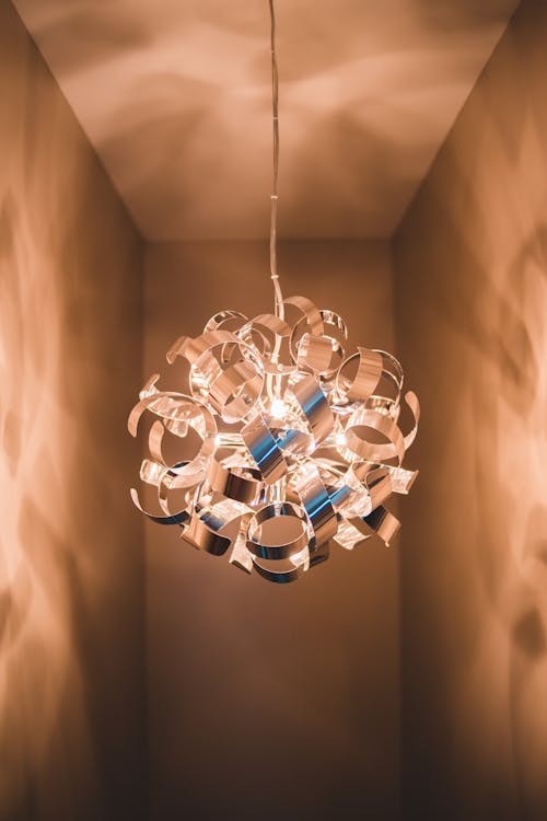 Creative shining spherical chandelier of curved elements hanging on long wire in narrow empty room