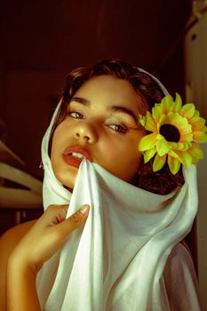 A striking portrait of a woman holding a sunflower, wrapped in a white shawl, evoking elegance and beauty.