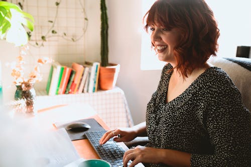 Free Woman Smiling while Typing Using an Apple Keyboard Stock Photo