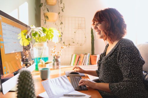 Free Woman comfortably working from home with plants on a sunny desk, showcasing modern technology. Stock Photo