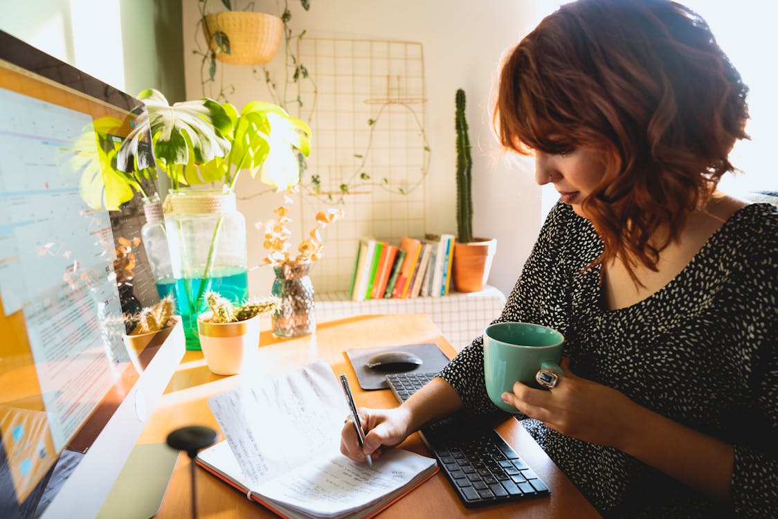 Free Woman Writing on Her Notebook while Holding a Cup Stock Photo