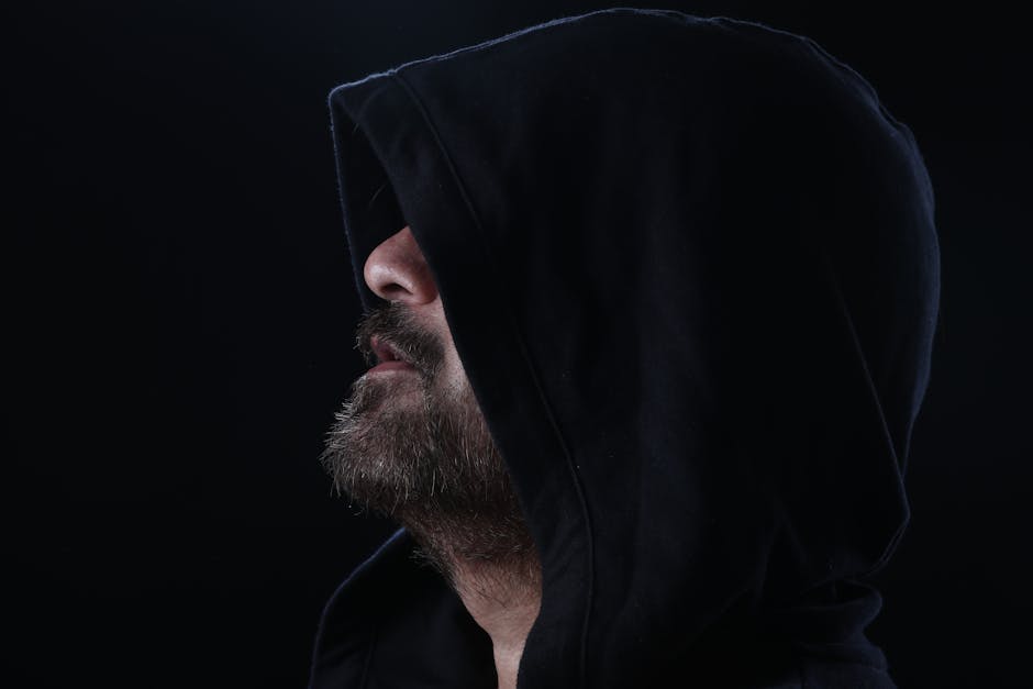 Side view of a bearded man in a hood, creating a mysterious and moody portrait in a studio setting.