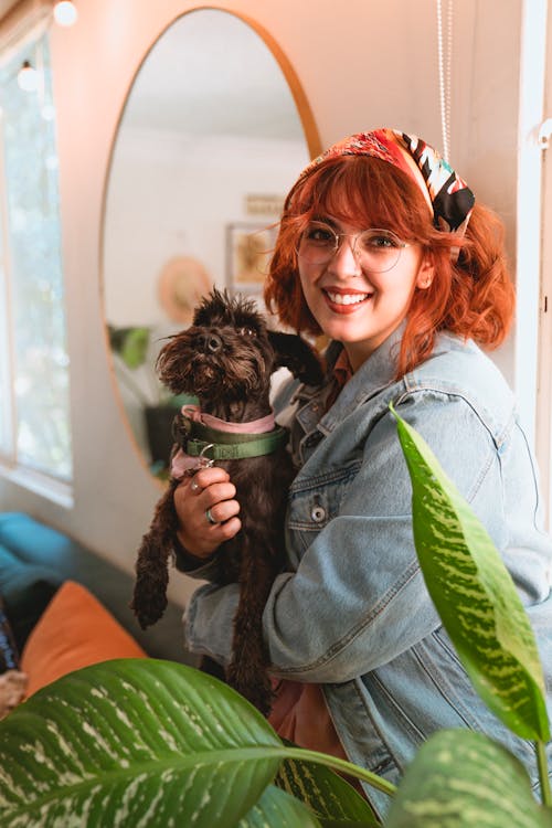 Woman in Light Blue Denim Jacket Smiling while Holding Her Dog