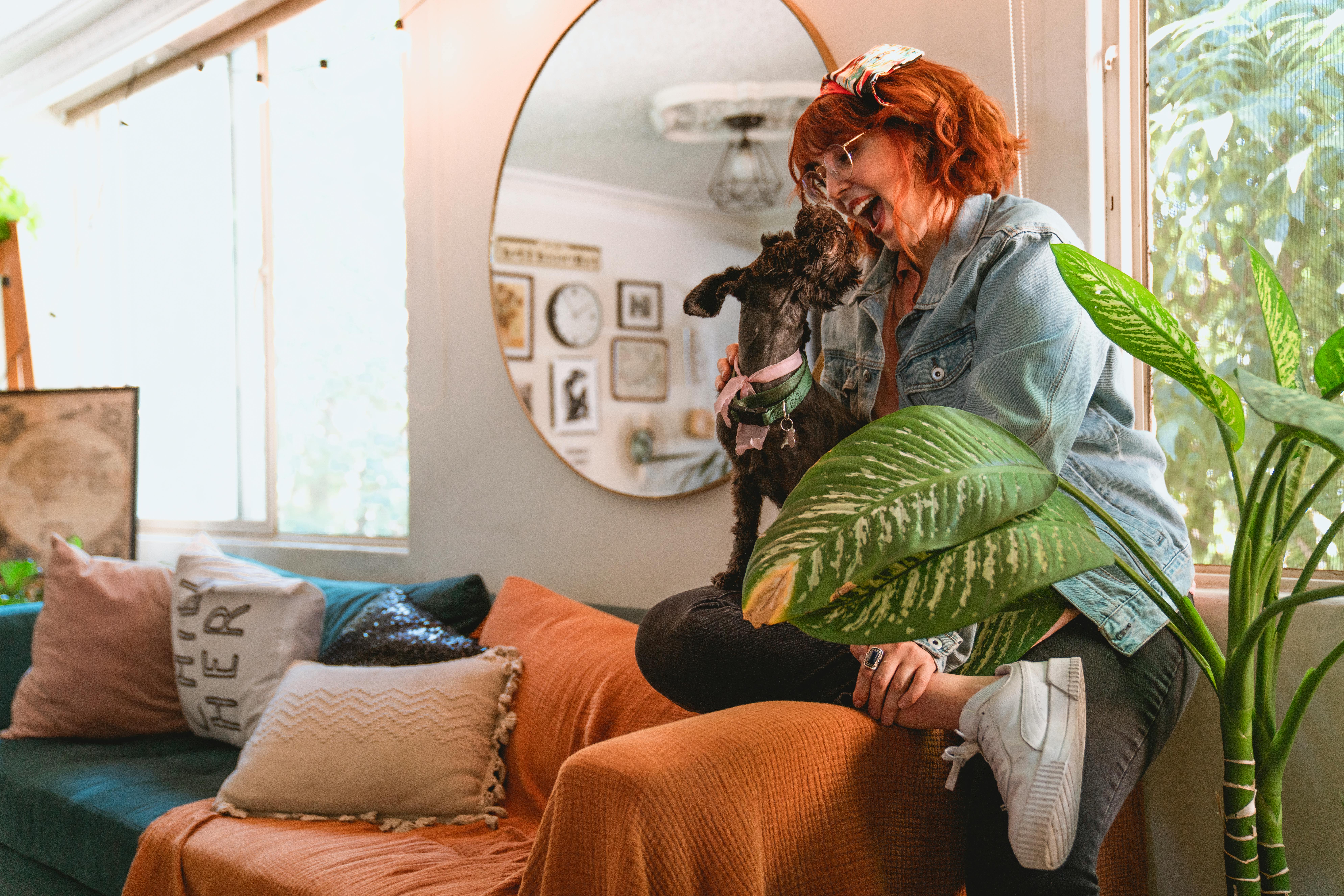 Smiling woman with red hair enjoys a playful moment with her dog on a cozy couch.