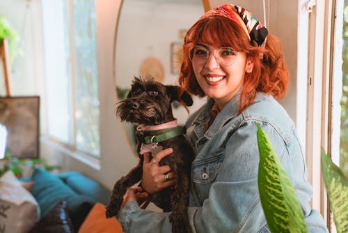 Woman in Light Blue Denim Jacket Smiling while Holding Her Dog