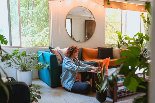 Woman working remotely from a cozy living room surrounded by plants.