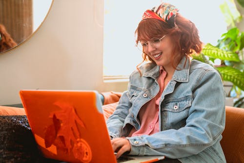 Woman in Denim Jacket Smiling while Using Her Laptop
