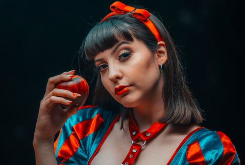 Free Young woman dressed as Snow White holding a red apple in a studio setting, evoking classic fairytale imagery. Stock Photo